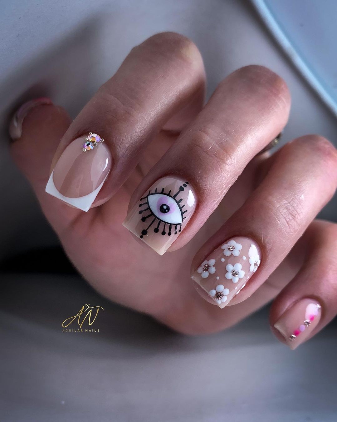 Varied Nail Art Featuring an Eye Design, White Florals, and a Jeweled Accent